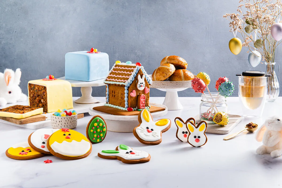 Spring-coloured cakes, iced Easter biscuits and a gingerbread house on a light table.