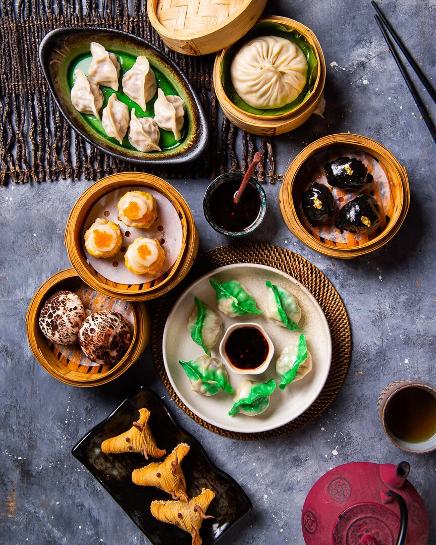 Dumplings and small dishes in bamboo steamers on a dark table.