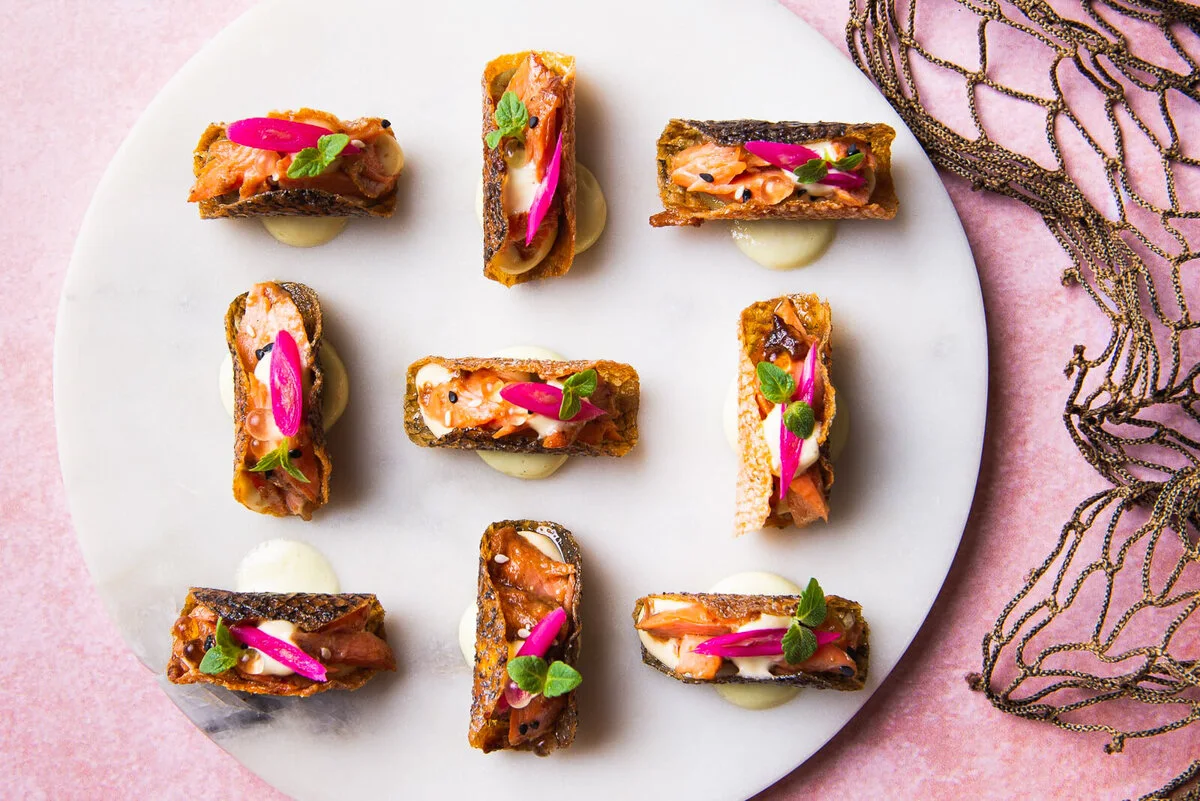 Small miso salmon tacos with colorful garnishes on a white surface.