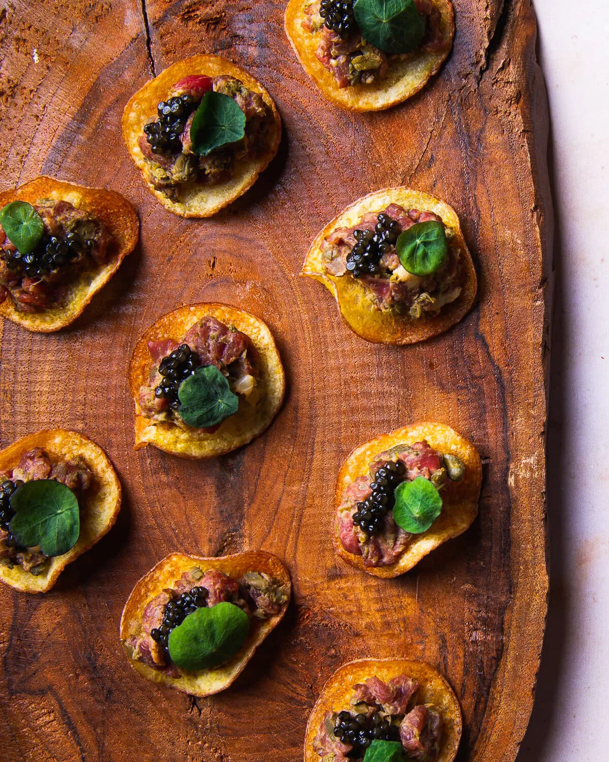 Beef tartare and caviar on potato crisps arranged on a wooden board.