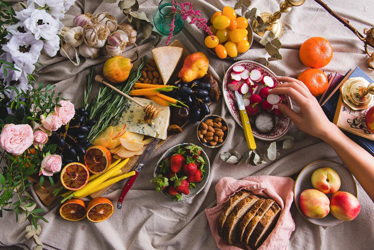 Hands reaching across an abundant grazing table with cheese, fruit and crackers.