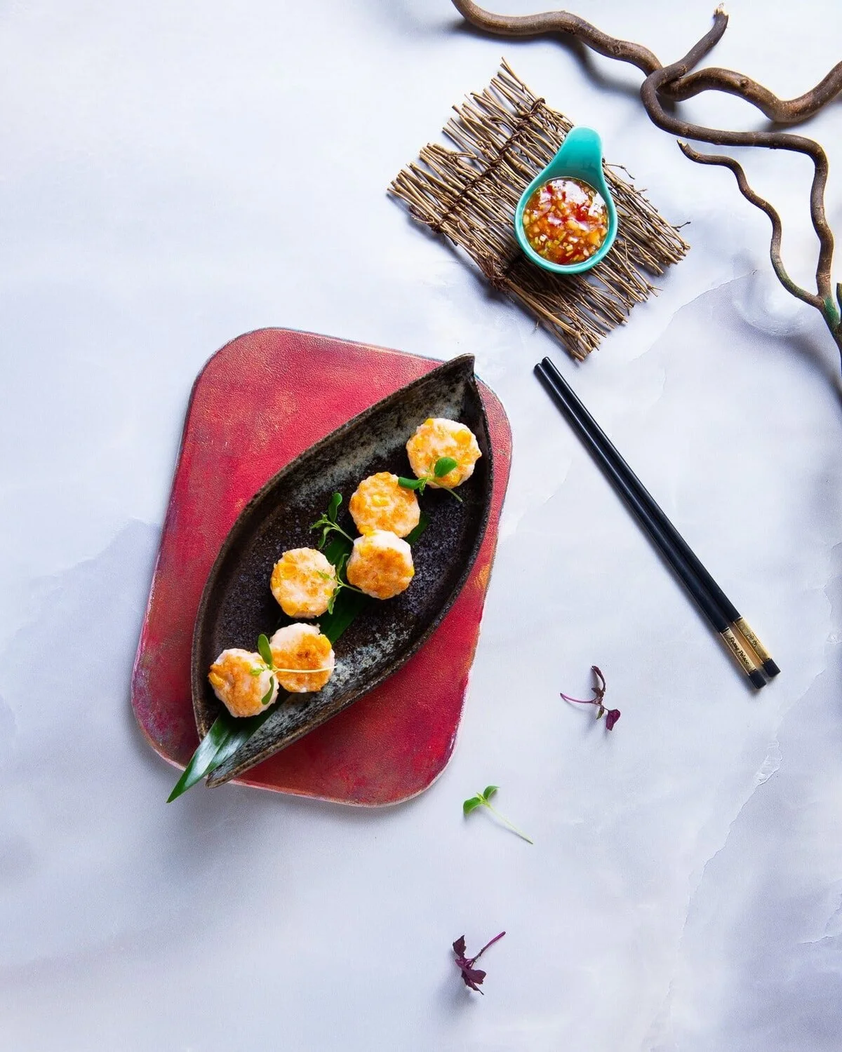 Round canapés arranged on a dark plate beside chopsticks.
