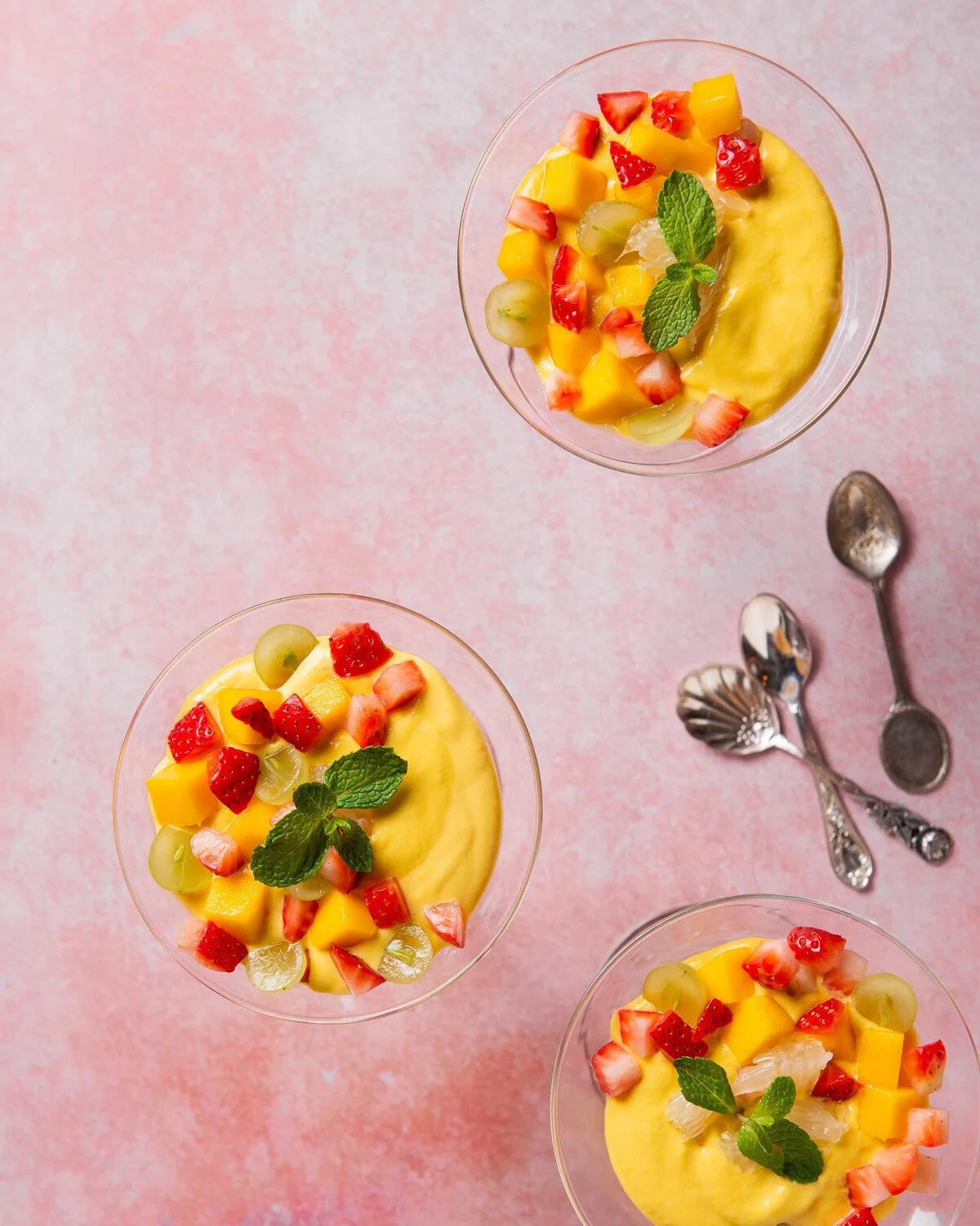 Overhead bowls of colorful fruit on a pink surface.
