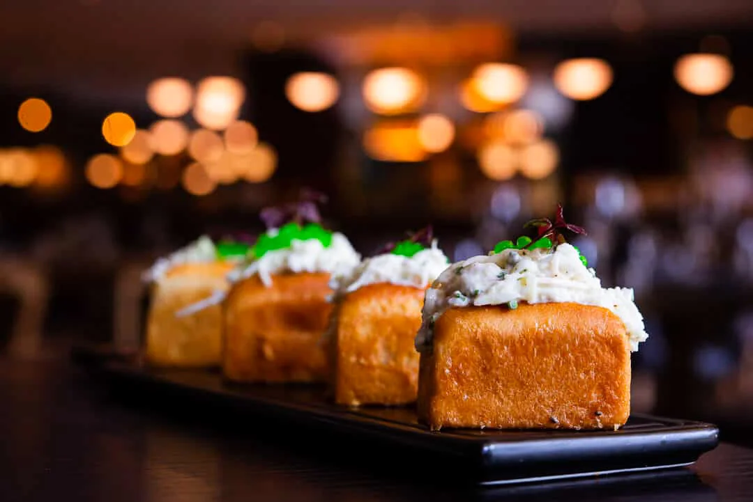 Golden bite-sized appetizers on a dark plate against warm lights.