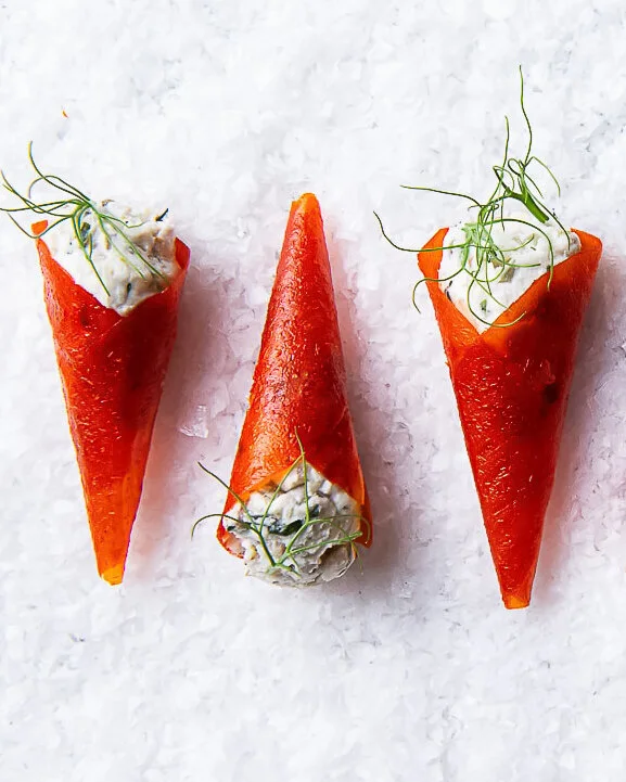 Orange canapé cones with pale filling on a white surface.