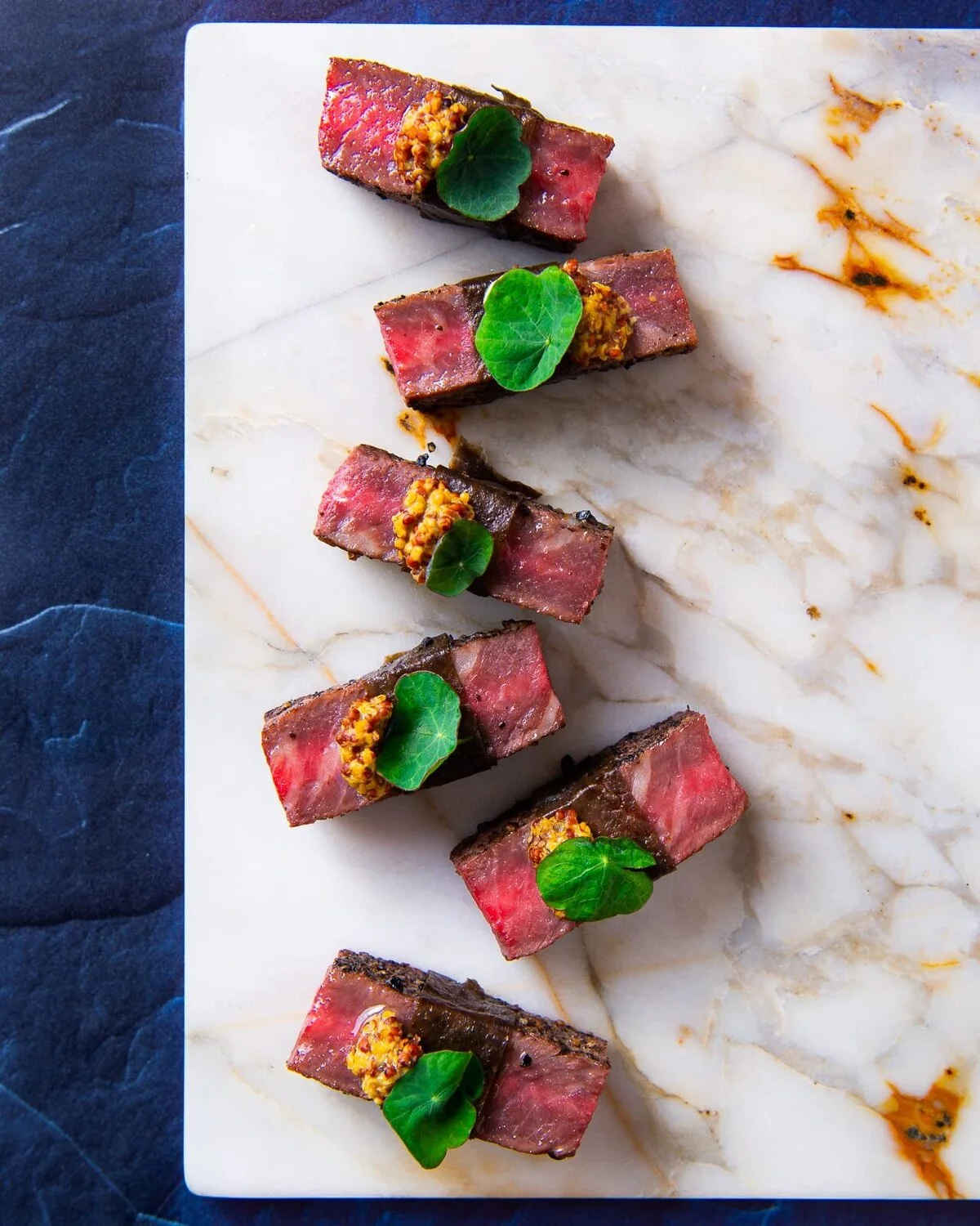 Seared Wagyu beef portions topped with green leaves on marble.