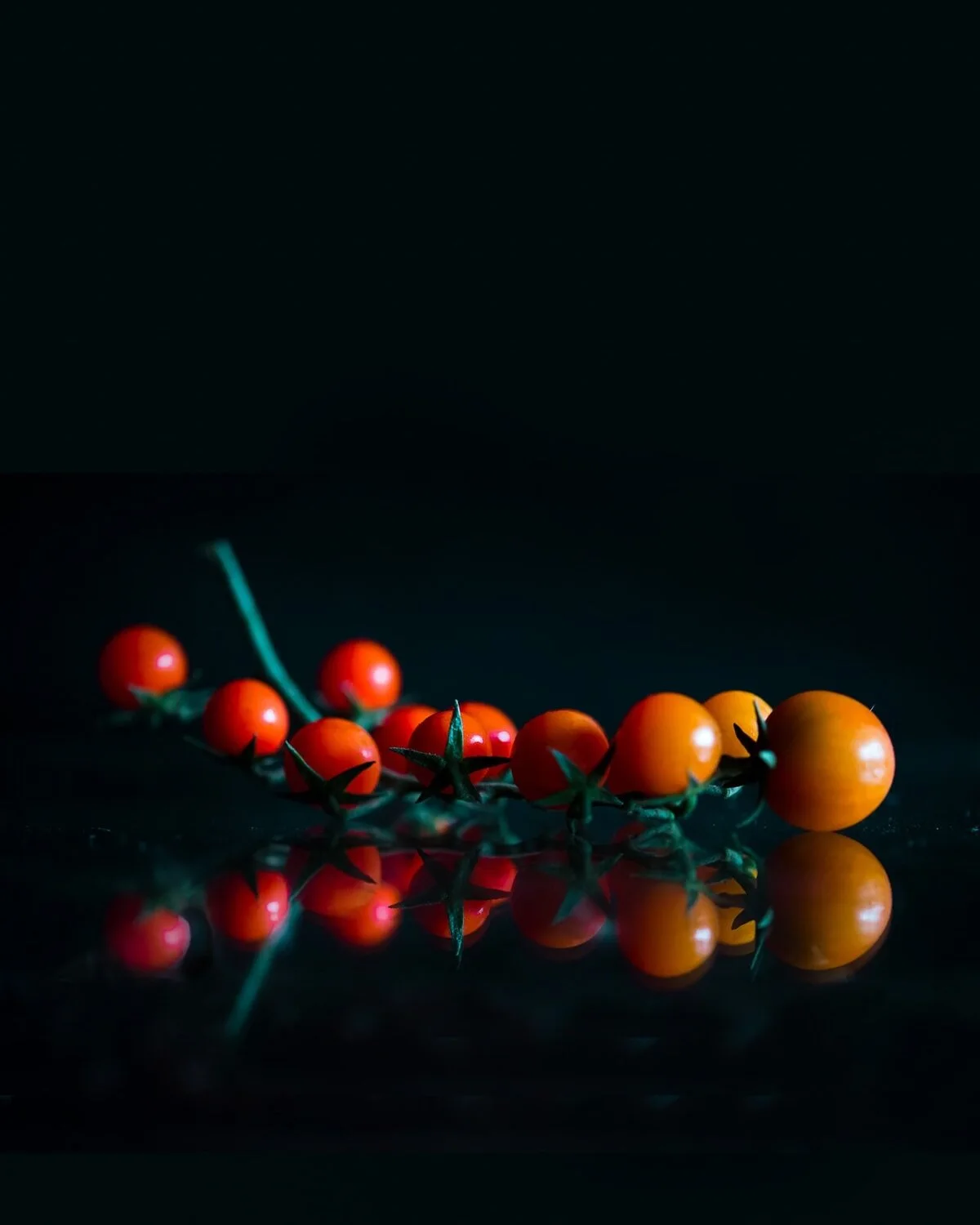 Red and yellow vine tomatoes reflected on a dark surface.