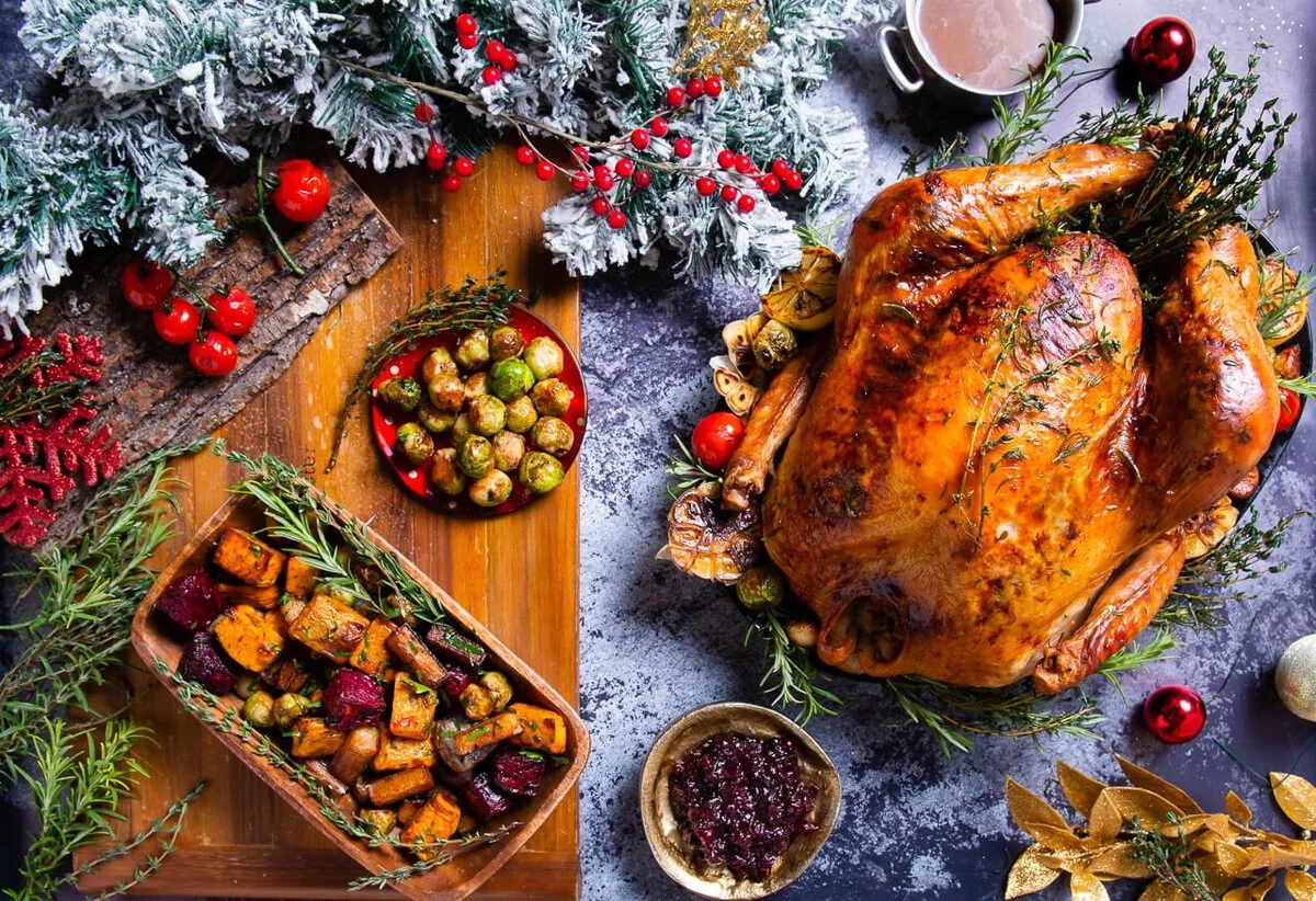 Overhead Christmas feast with roast turkey, side dishes and festive greenery.