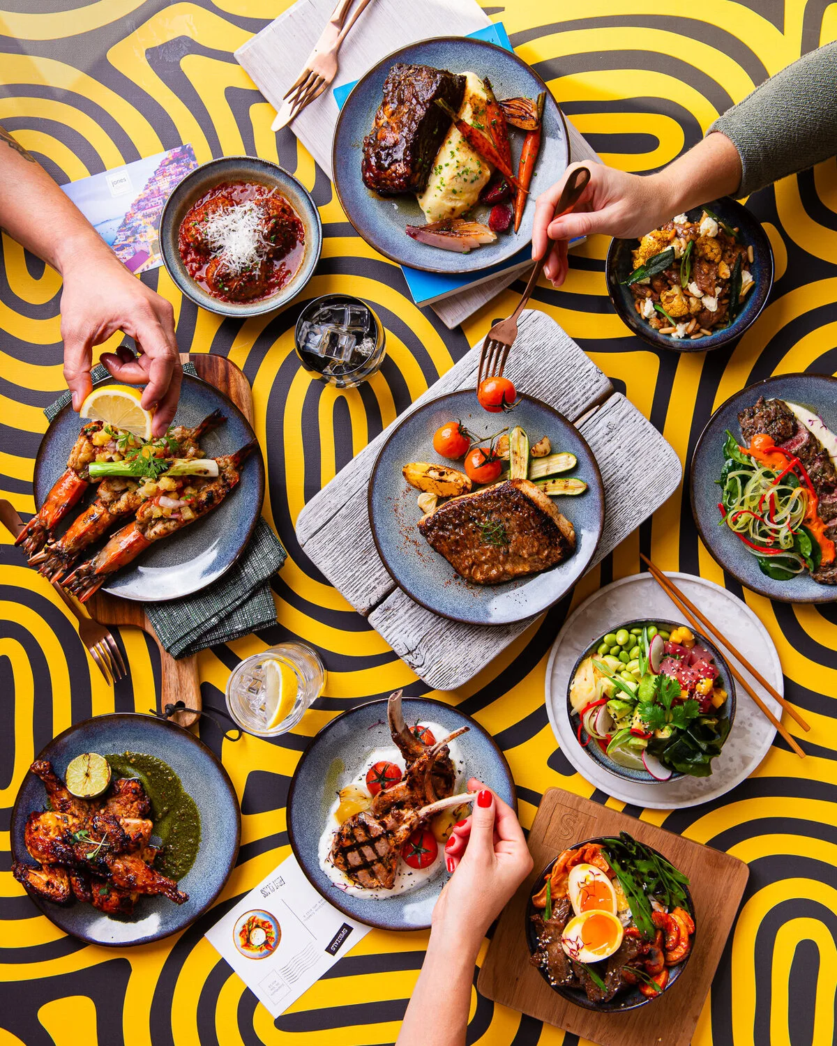 Overhead restaurant feast on a bright yellow patterned table.