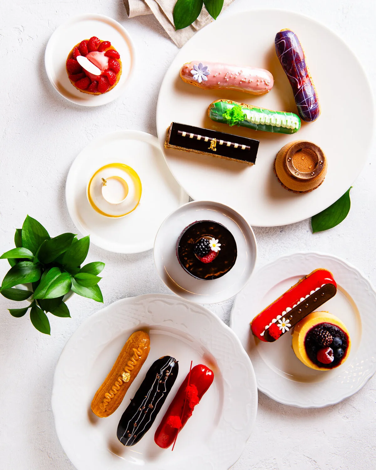 Colorful éclairs and small desserts arranged on white plates.