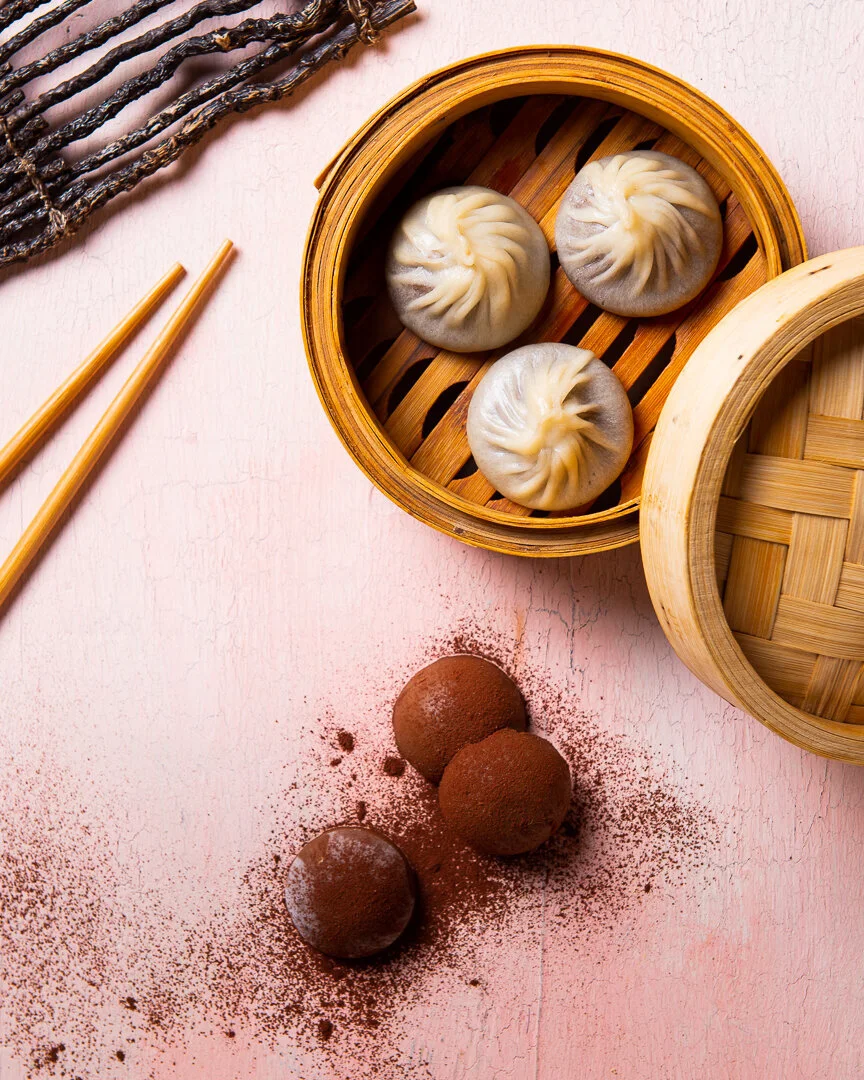 Dumplings in bamboo steamers on a pink tabletop.