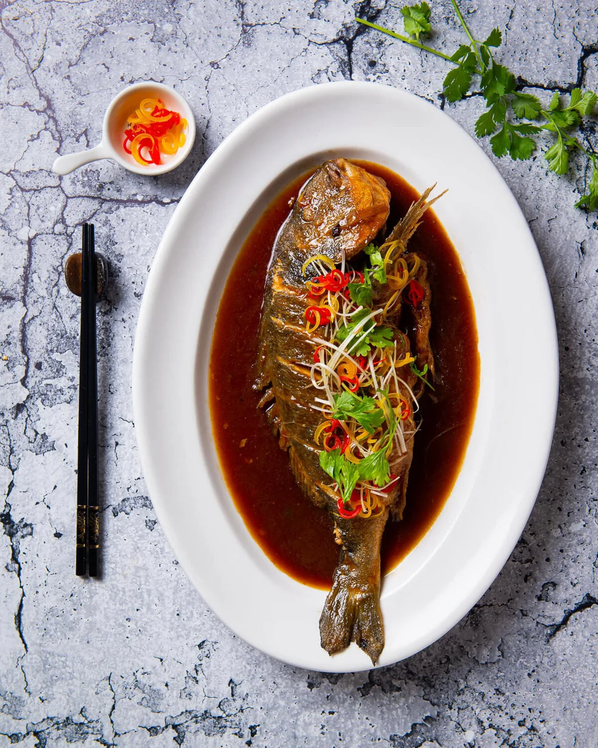 Braised sea bream on an oval platter with sauce and herbs.