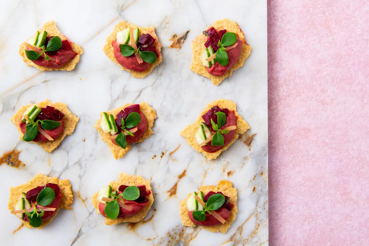 Falafel and beetroot hummus canapés with pickled cucumber on a white slab.