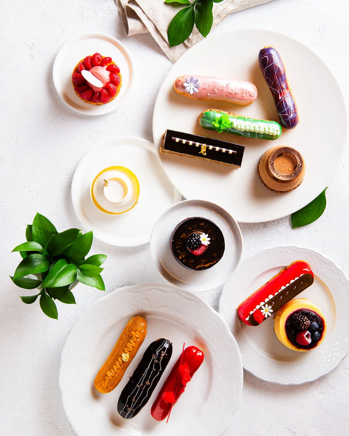 Colorful éclairs and small desserts arranged on white plates.