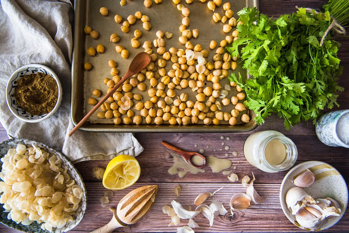 Overhead arrangement of chickpeas, herbs, lemon and preparation utensils.