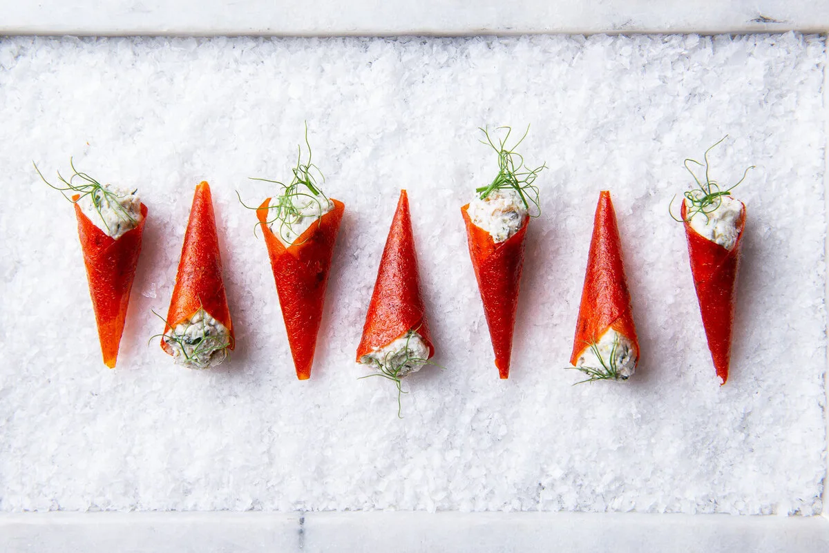 Orange canapé cones with pale filling arranged on a white surface.