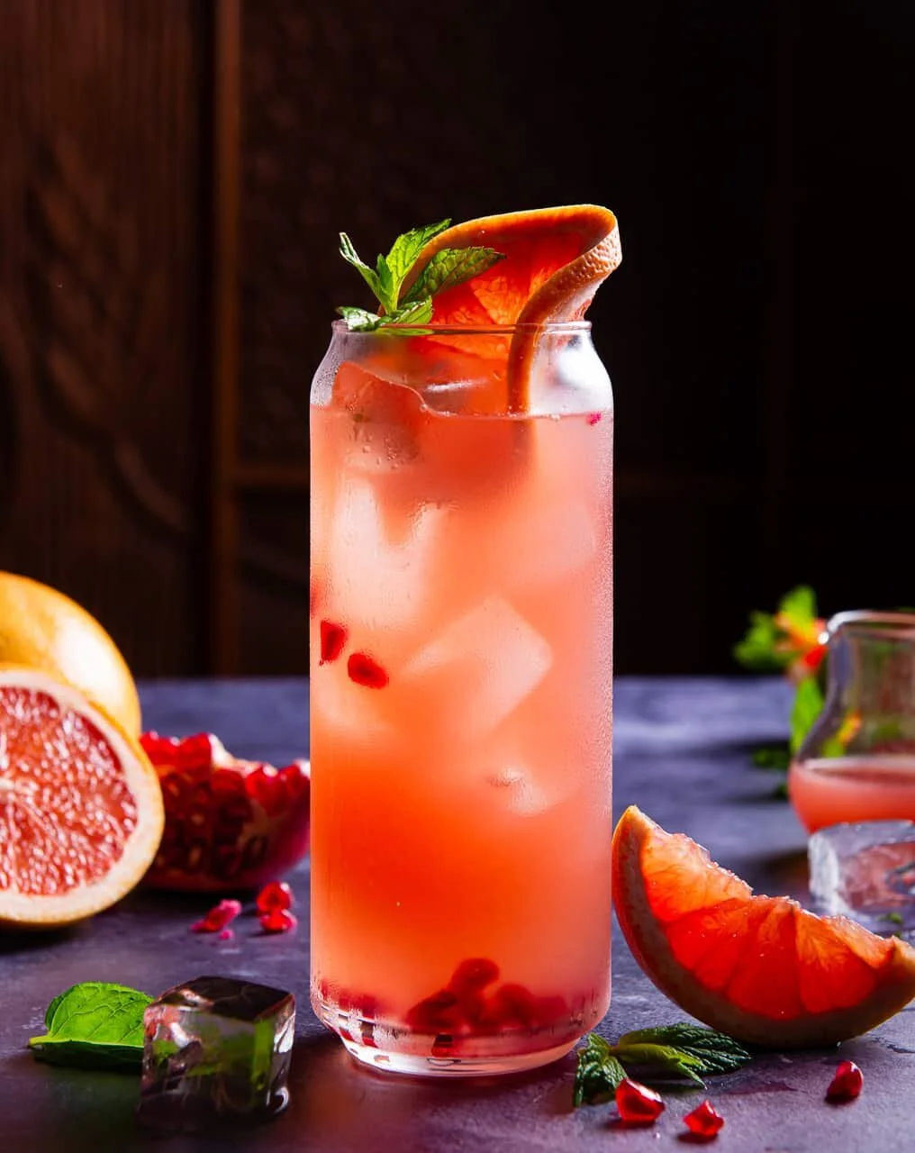 Tall pink cocktail with a citrus garnish on a dark wooden table.