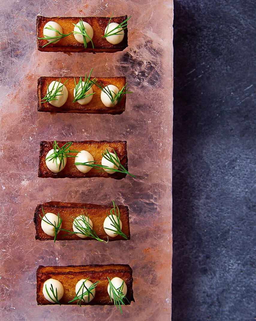 Five rectangular canapés topped with green leaves on a wooden board.