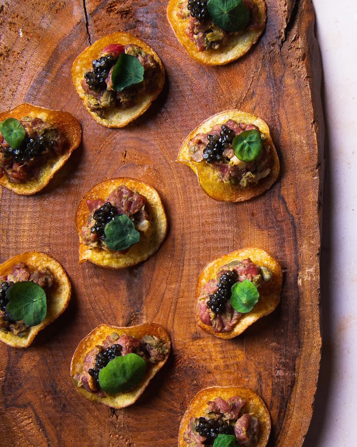 Beef tartare and caviar on potato crisps arranged on a wooden board.